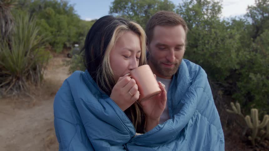 Couple snuggled in a blanket drinking from a copper mug outdoors