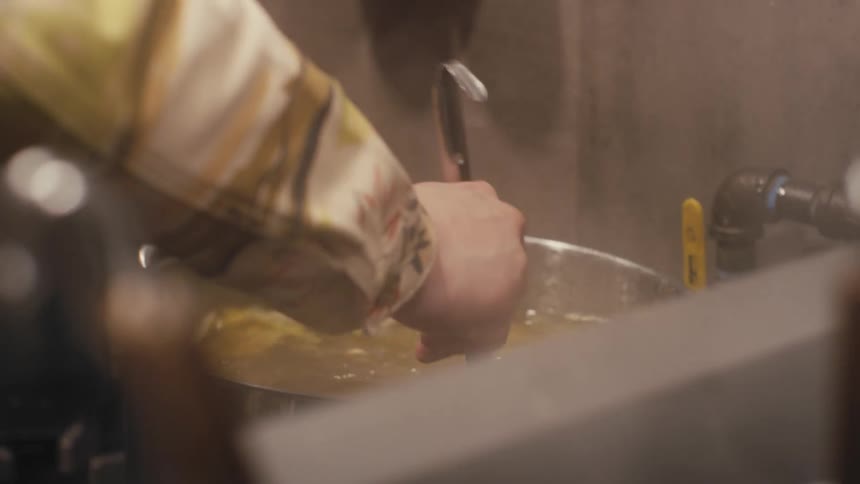 Chef's hand stirs a steaming pot of soup