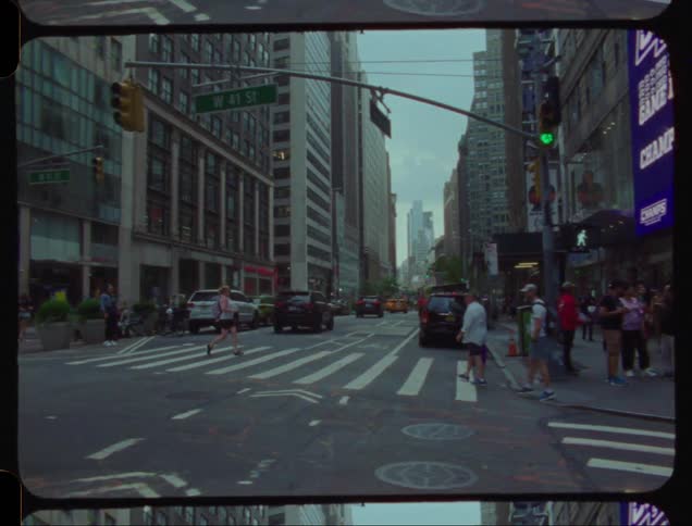 A small crowd of people walk across a crosswalk in the middle of a busy city street with traffic and buildings