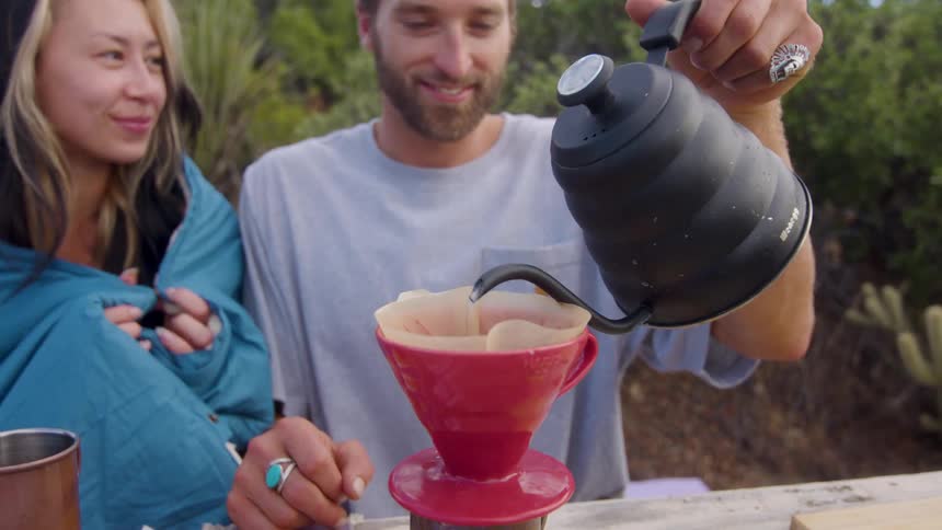 A man is pouring hot water into a filter outside for coffee