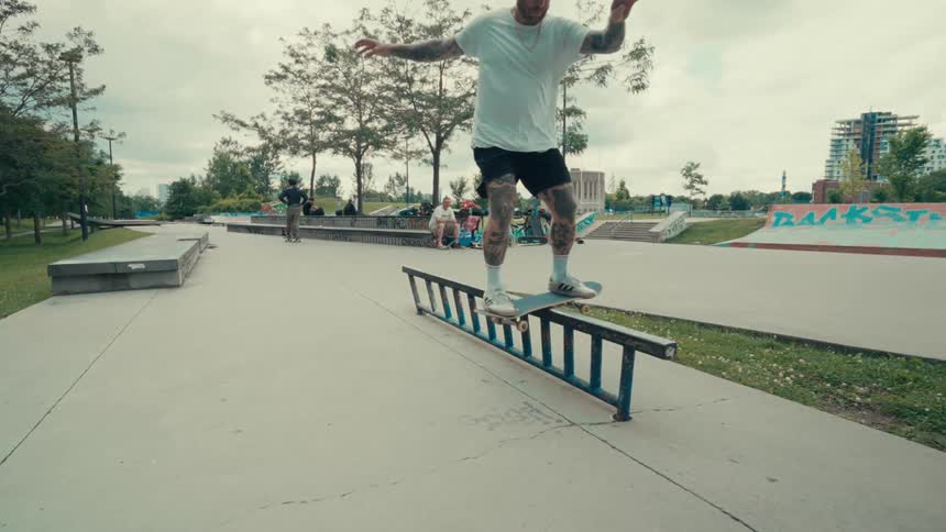 A skateboarder man is doing a trick with his skateboard sliding over a large piece of pipe on the ground