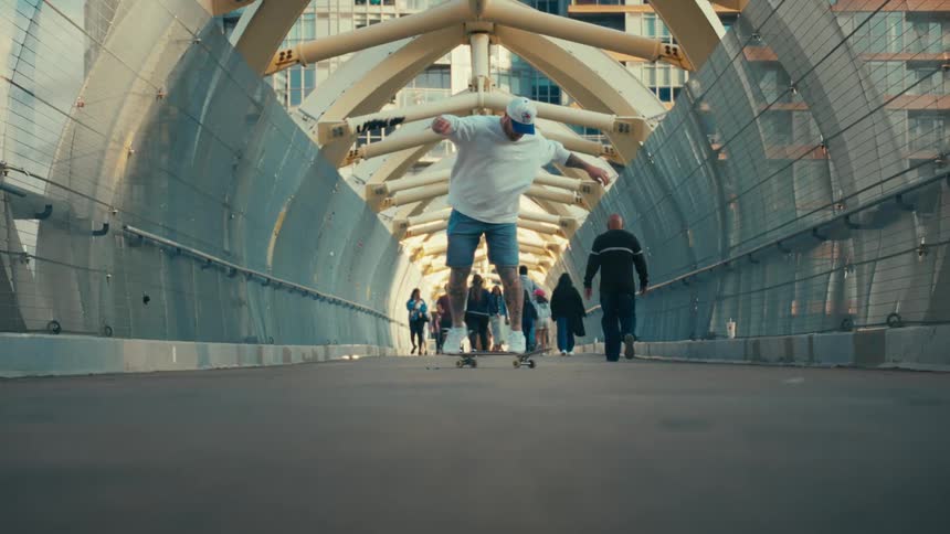 People walking on a bridge and a man doing tricks on a skateboard