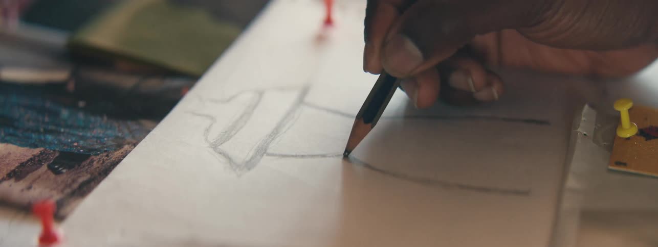 Hand of an illustrator with a pencil drawing the silhouette of a dress