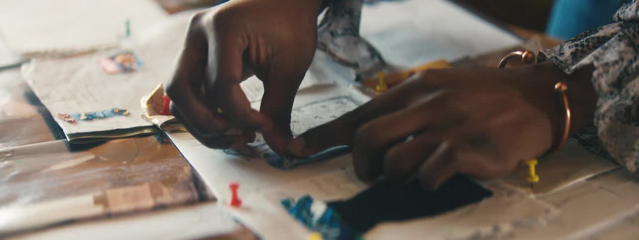Pair of womans hands placing dress fabrics in designs on table