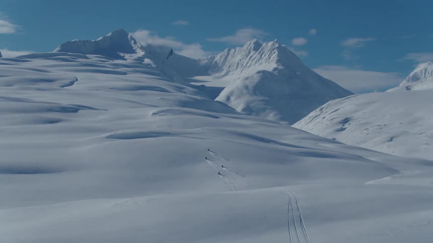 A group of snowmobiles traverse a snow covered mountain valley