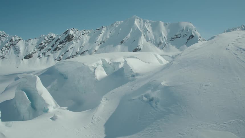 Aerial view of snowcapped mountains with a massive glacier in the foreground and a clear blue sky above