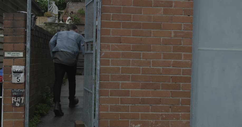 A man walks through a gate, checks his mail and pics up his paper