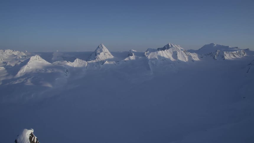 Aerial view of a vast field with layers of snow and mountains
