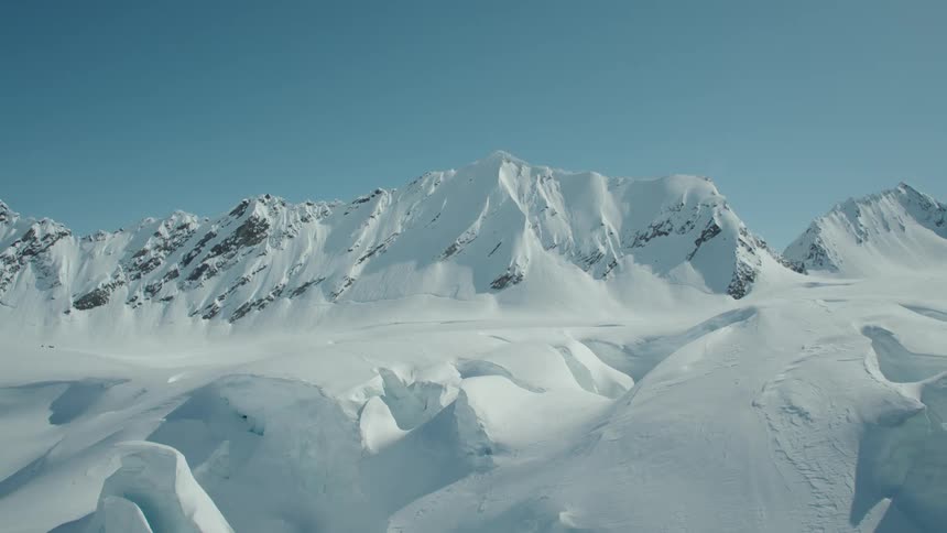 Aerial of snow capped mountain peaks under blue skies