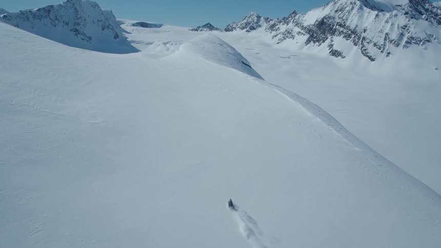 Person rides a snowmobile across a snow covered slope near the mountains on a winter day