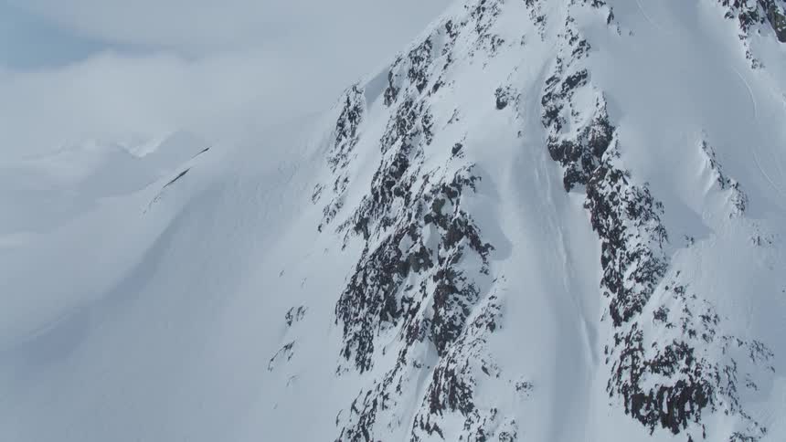 Aerial view of a person snowboarding down a large mountain with layers of snow
