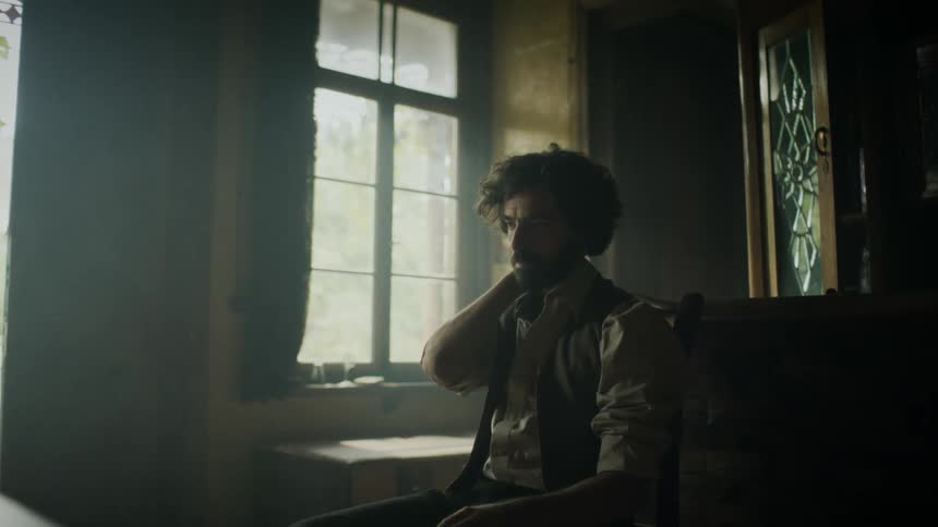 A lonely man sits on a dimly lit room with a candle sitting on a table in front of him