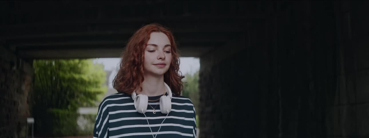 A woman is wearing headphones under the overpass