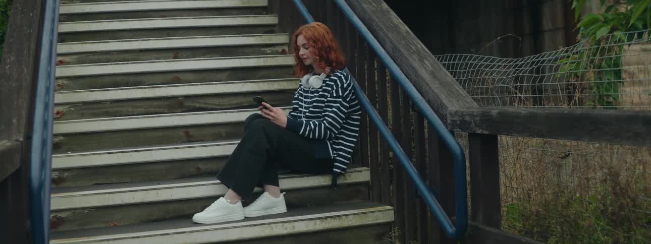 Woman with red hair in a striped shirt sitting on steps texting on cell phone