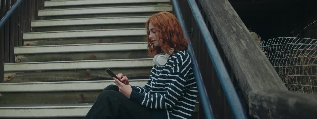 Red haired female sitting on steps outside a building scrolling on cell phone