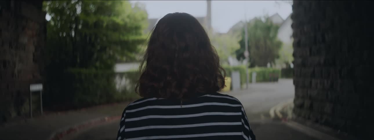 Redheaded woman walks through a tunnel on a residential street during daytime