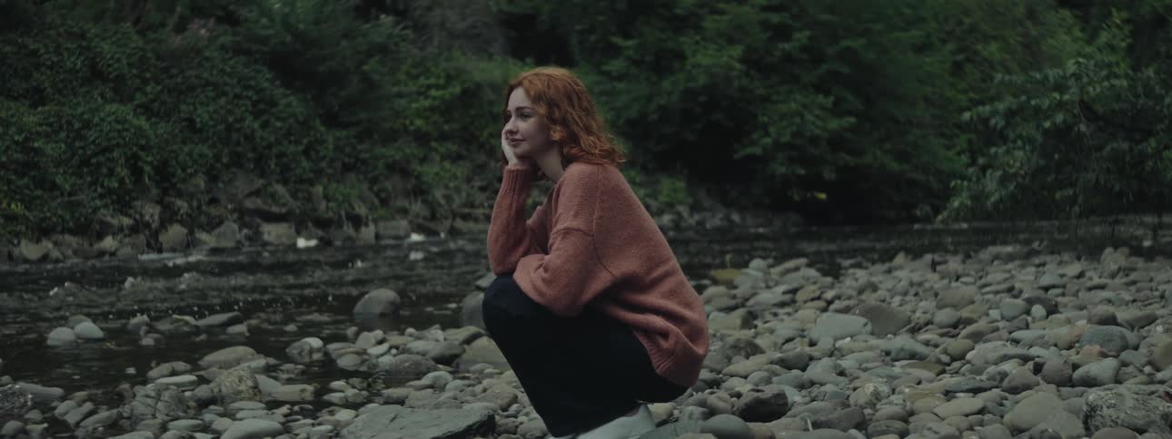 Woman crouching down on rocks watching the creek in the wilderness