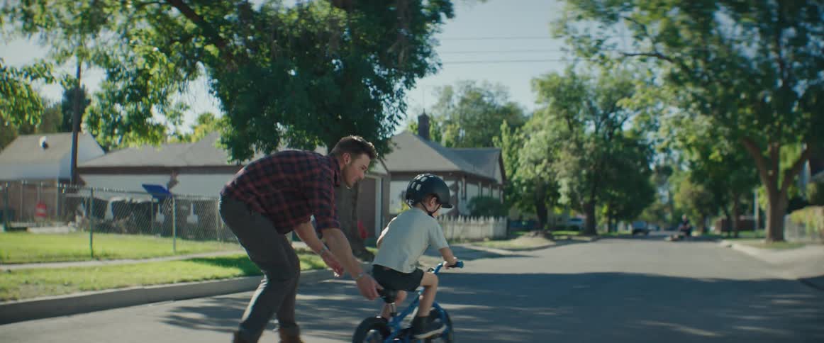 A father walks alongside his son as he learns to ride a bike