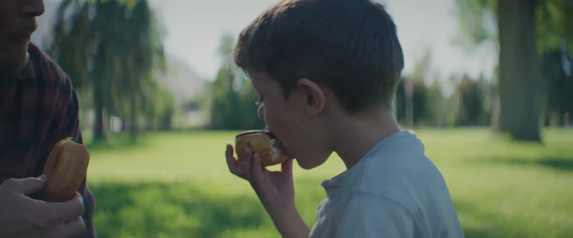 A father and son eat doughnuts in a park