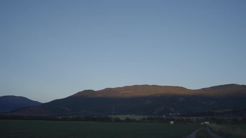 A serene landscape at dusk with rolling hills a distant town and a vast field bathed in the soft light of the setting sun