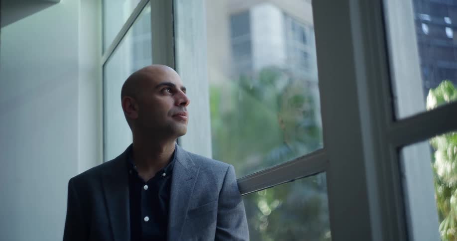 Office worker wearing a suit stares out the window of an office building downtown