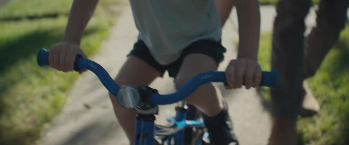Adult person helping a child to ride a bike