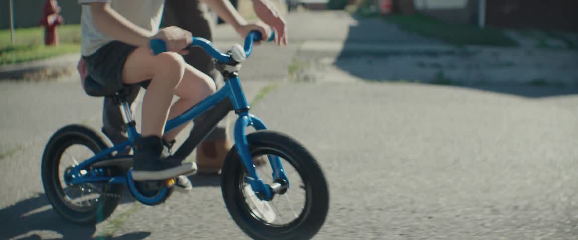 A father teaches his son how to ride a bike on a street in a suburb