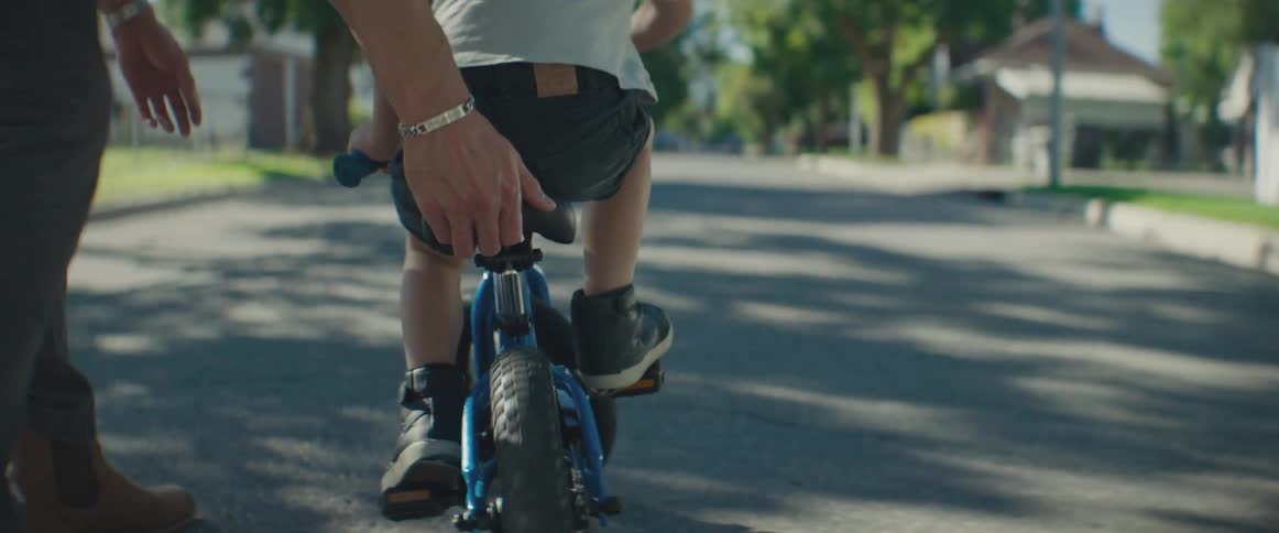 Father resting his hand on his sons bike as he learns to ride