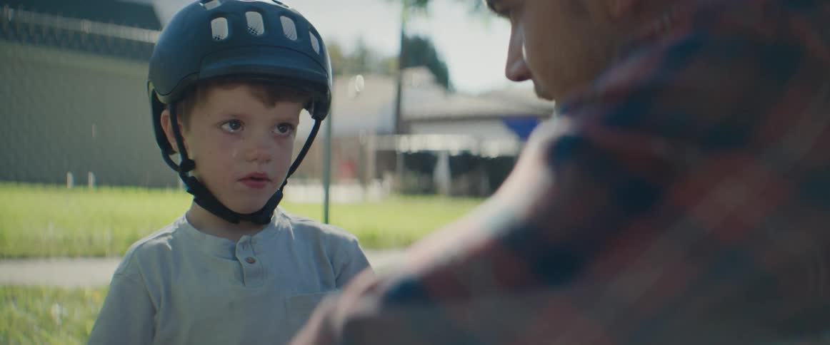 Father talking to his son who is wearing a helmet in an outdoor setting