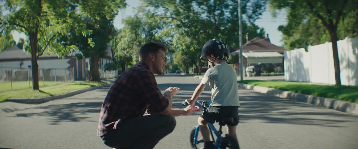 Father crouches to give his son instructions on how to ride a bicycle