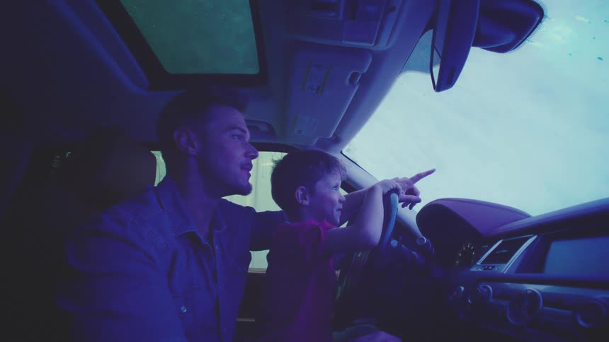 Boy having fun with his father inside the car while the car is being washed by a machine
