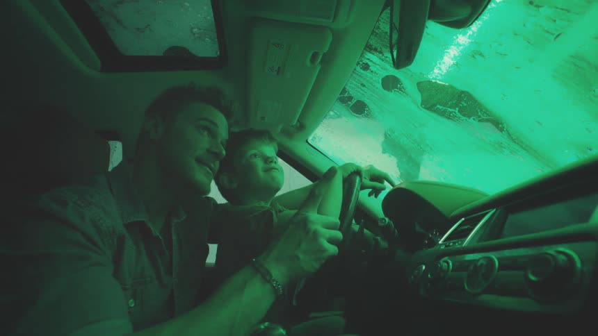 Father lets his son sit behind the wheel while the vehicle goes through the car wash