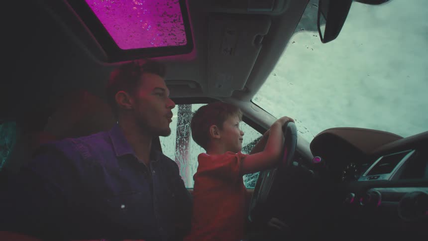 Boy having fun with his father inside the car while the vehicle is being washed on its exterior in a machine