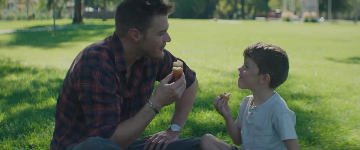 Father and son sitting on the grass talking and eating and smiling