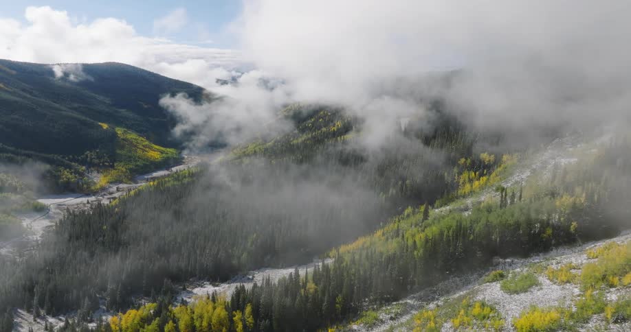 Low lying clouds float over patches of deciduous and conifer woods covering snowy mountain slopes on a winter day