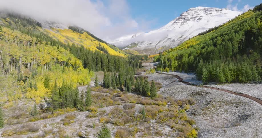 Aerial of train tracks running through a valley in a mountain range on an autumn day