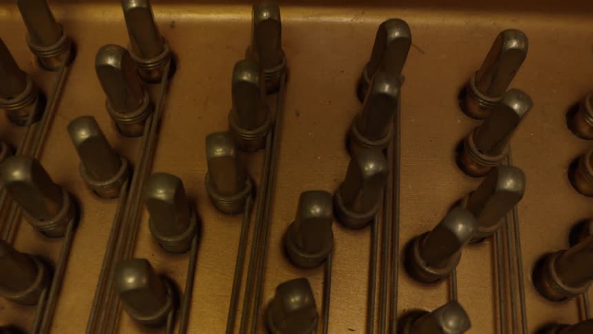 The innards of a keyboard powered musical instrument with wires stretched to metal pegs to hold them in place