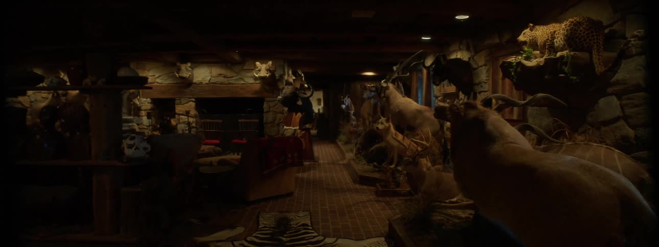 A dimly lit room with walls adorned with mounted animal heads and skins creating a rustic and somewhat eerie atmosphere