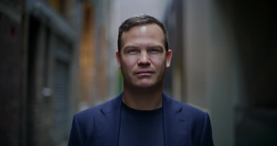 Man in a narrow alley between buildings stares straight ahead