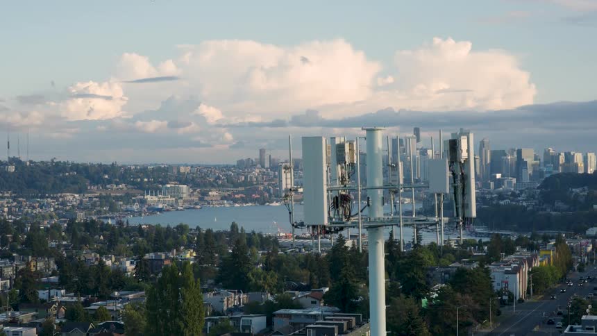Ascending along and over the top of a cellular transmission tower with a large metro area in the distance