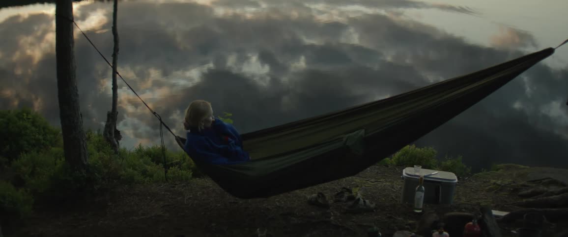 Woman lying in a green hammock next to a lake reflecting the sky