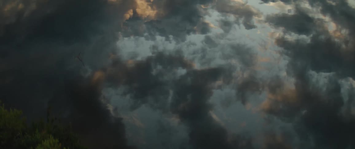 A dramatic sky filled with dark swirling clouds illuminated by the setting sun reflected on a lake