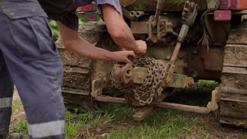 A person putting a chain behind a tractor that is full of mud