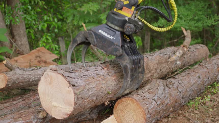 A tractor with a grapple picking up a tree trunk and placing it in a pile