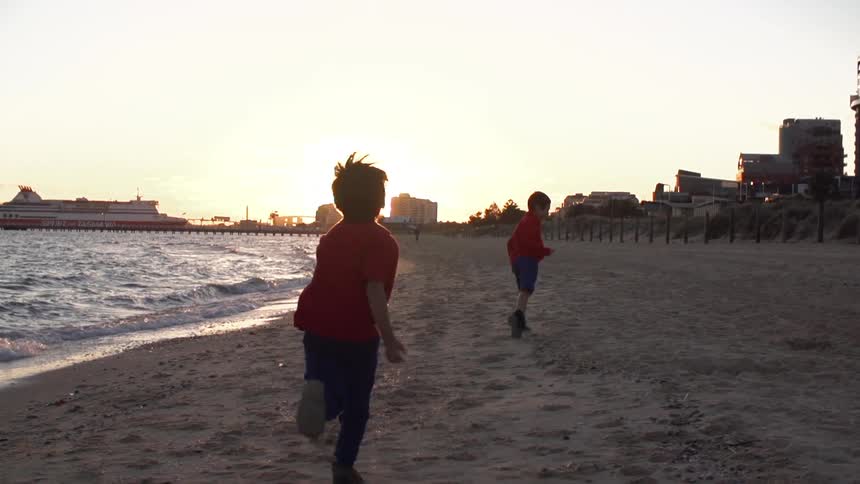 Boys run on a beach at sunset