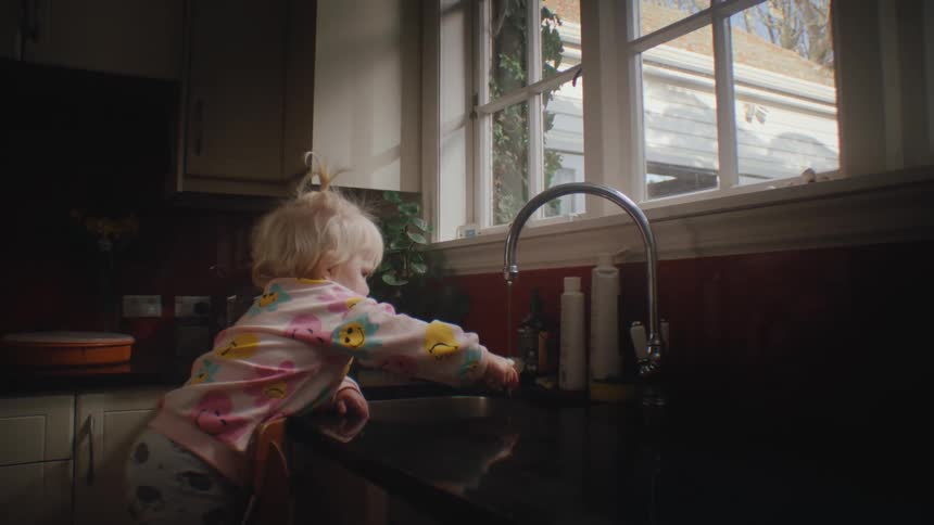 Little girl wets her toothbrush under the kitchen sink and puts it in her mouth