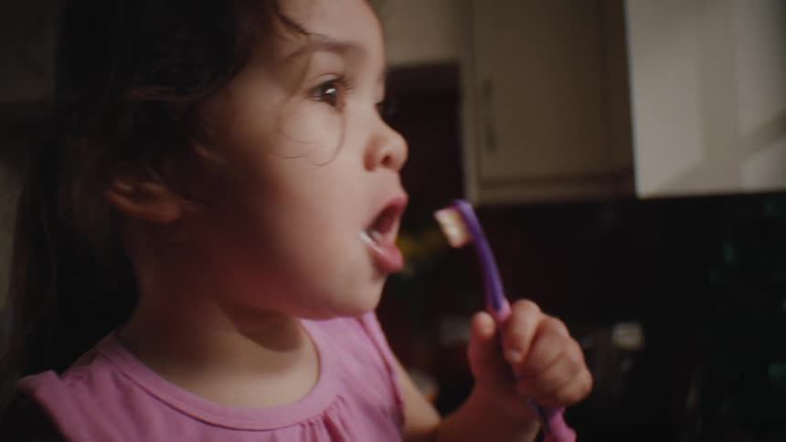 Young girl uses a purple and pink toothbrush to brush her teeth