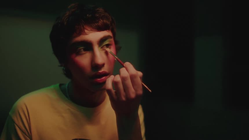 The face of a young man who is using a brush to apply makeup to his eyes