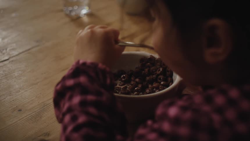 Little girl sitting at the table eating a bowl of cereal with milk