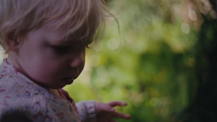 Little blonde girl holding a yellow flower in a garden